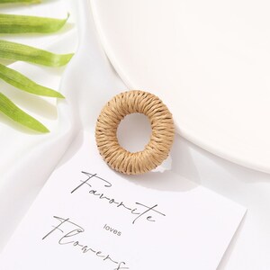 May include: A round, woven, beige-colored object with a hole in the center. The object is on a white surface with a white plate and a card that reads "Favorite Flowers". A green leaf is in the background.
