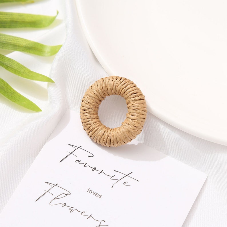 May include: A round, woven, beige-colored object with a hole in the center. The object is on a white surface with a white plate and a card that reads "Favorite Flowers". A green leaf is in the background.