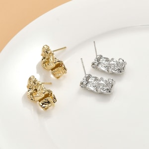 Peut inclure: Une paire de boucles d'oreilles avec un design texturé et irrégulier. Une boucle d'oreille est dorée et l'autre est argentée.