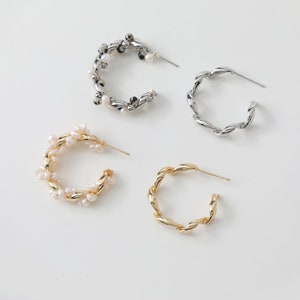 Pode incluir: Três pares de brincos de argola. Um par é de prata com pequenas pérolas brancas, um par é de ouro e um par é de prata com um design torcido.