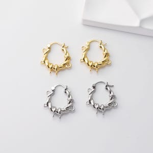 Peut inclure: Quatre boucles d'oreilles créoles, deux dorées et deux argentées, sont présentées sur fond blanc. Les boucles d'oreilles ont un design torsadé avec de petits accents pointus. Les boucles d'oreilles dorées sont en haut, et les argentées en bas.