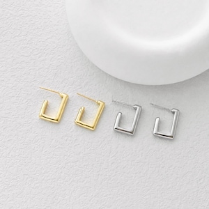 Può includere: Una collezione di orecchini a cerchio quadrati in oro e argento. Gli orecchini sono esposti su una superficie bianca. Gli orecchini hanno un design minimalista, con un perno e una forma quadrata.