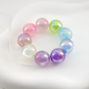 May include: A strand of iridescent pastel beads in pink, purple, blue, green, and white. The beads are strung on a clear elastic cord.