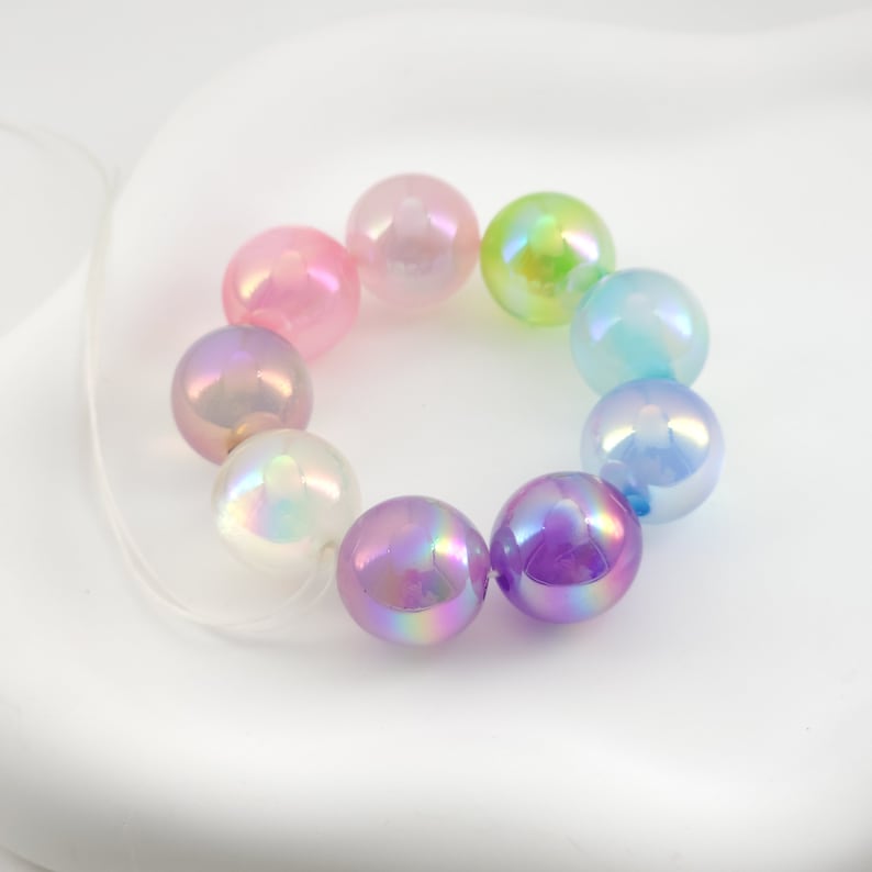 May include: A strand of iridescent pastel beads in pink, purple, blue, green, and white. The beads are strung on a clear elastic cord.
