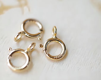 May include: Three gold-colored spring ring clasps. The clasps are round with a small loop and a spring mechanism for secure closure. The clasps are likely for jewelry making or repair.