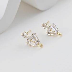 May include: A pair of gold-tone earring findings with clear crystal accents. The findings have a hook closure.