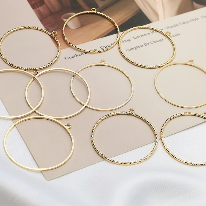 May include: Eight gold-colored metal hoops of varying sizes. Some hoops have a textured surface, while others are smooth. All hoops have a small loop at the top.