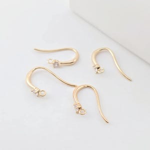 May include: Four gold-toned earring hooks with a clear crystal at the top of each hook.