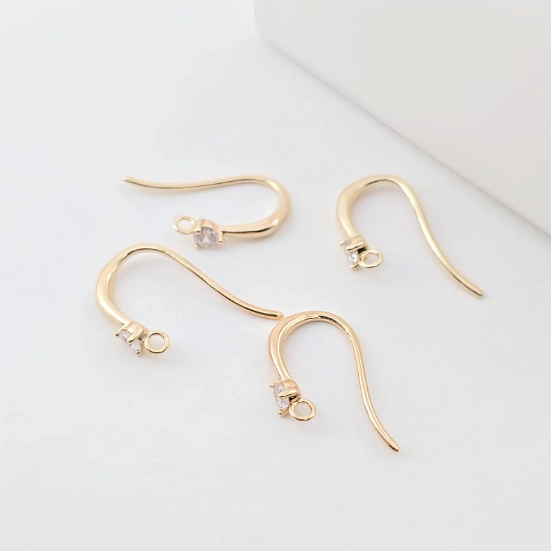 May include: Four gold-toned earring hooks with a clear crystal at the top of each hook.