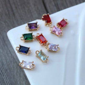 May include: Assortment of colorful rectangular connector charms with gold-toned metal settings. The charms feature various colors including red, pink, green, blue, purple, and clear.