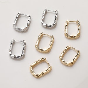 Pode incluir: Seis pares de brincos de argola de prata e ouro com uma forma irregular texturizada. Os brincos são todos do mesmo tamanho e forma, mas de cores diferentes.
