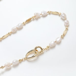 May include: A gold chain necklace with white baroque pearls and a gold clasp.