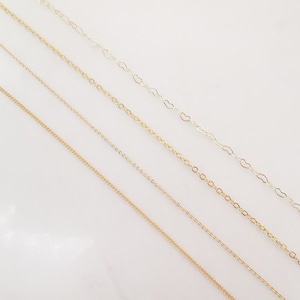 May include: Four gold chains of different styles and thicknesses, laid out on a white surface.