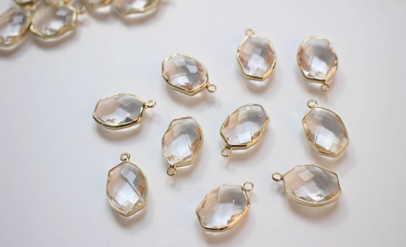 K&ouml;nnte beinhalten: Zehn klare, ovale Glasschmuckst&uuml;cke mit goldfarbenen Metallrahmen und &Ouml;sen. Die Charms sind facettiert und haben einen dezenten Schimmer.