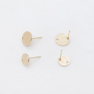 Peut inclure: Quatre boucles d'oreilles à clous dorées avec un motif circulaire texturé. Chaque boucle d'oreille a une tige pour l'insertion et un petit trou pour fixer le fermoir. Les boucles d'oreilles sont présentées sur un fond blanc.
