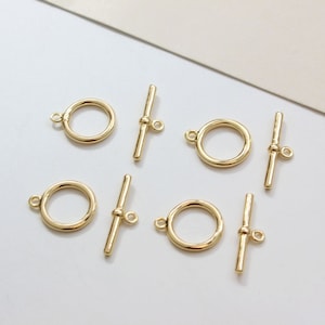 Peut inclure: Six fermoirs à bascule en métal doré, chacun avec un anneau rond et une barre droite. Ces fermoirs sont couramment utilisés pour la fabrication de bijoux et l'artisanat.