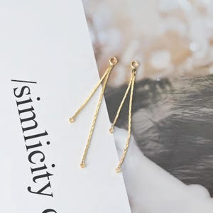 Peut inclure: Une paire de boucles d'oreilles pendantes dorées avec un design délicat de chaîne. Chaque boucle d'oreille a trois brins de chaîne qui sont reliés en haut et en bas.