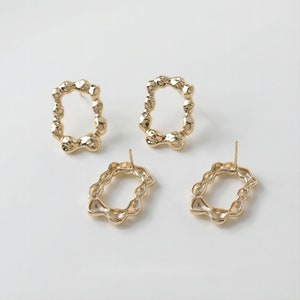 May include: A pair of gold-toned earrings with a unique, textured, irregular oval shape. The earrings have a post back closure.