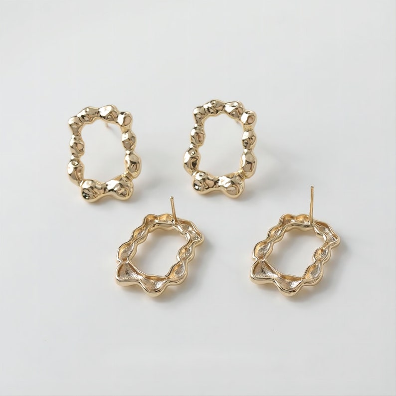 May include: A pair of gold-toned earrings with a unique, textured, irregular oval shape. The earrings have a post back closure.