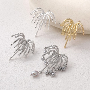 May include: Four decorative earrings in silver and gold tones. The earrings have a textured, palm frond design. One pair of silver earrings has small gray pearl accents. The earrings are displayed on a white surface.