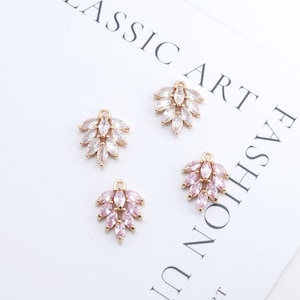 Op de afbeelding: Vier goudkleurige metalen bedels met heldere en roze kristallen accenten. Elke bedel heeft een cluster van marquise-vormige kristallen die in een bladvormig ontwerp zijn gerangschikt.