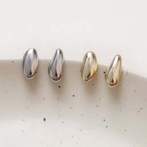 May include: Three pairs of minimalist earrings in silver, gold, and rose gold. Each earring is a smooth, oval shape.