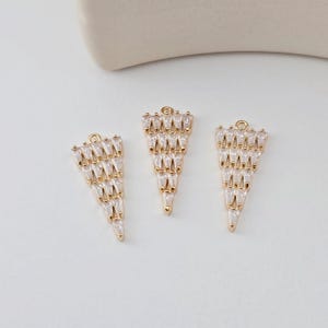 May include: Three gold triangle-shaped pendants with clear crystal embellishments. Each pendant features a cascading design of small, pointed crystals.