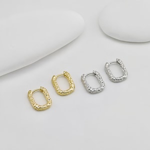 May include: Three pairs of textured oval hoop earrings. The earrings are shown on a white surface. One pair is gold, one pair is silver, and one pair is a mix of gold and silver.
