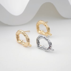 May include: Two pairs of earring findings in gold and silver. The findings are shaped like an irregular oval with a textured surface. Each finding has a small loop at the bottom for attaching a charm or pendant.