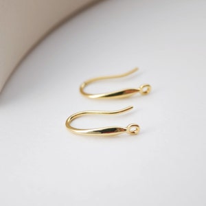 May include: Two gold-toned earring hooks. The hooks are made of metal and have a smooth, curved shape.