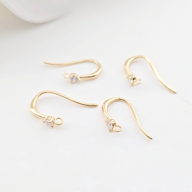 May include: Four gold-toned earring hooks with a small clear rhinestone at the top of each hook.