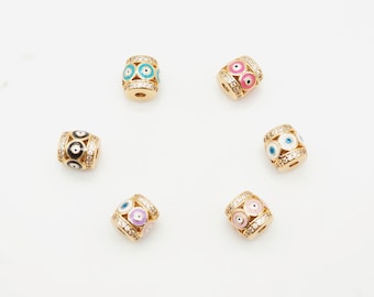 May include: Six gold-toned barrel-shaped beads with an evil eye design. Each bead has a different colored enamel background: black, blue, pink, white, light pink, and light blue. The beads are decorated with clear rhinestones.