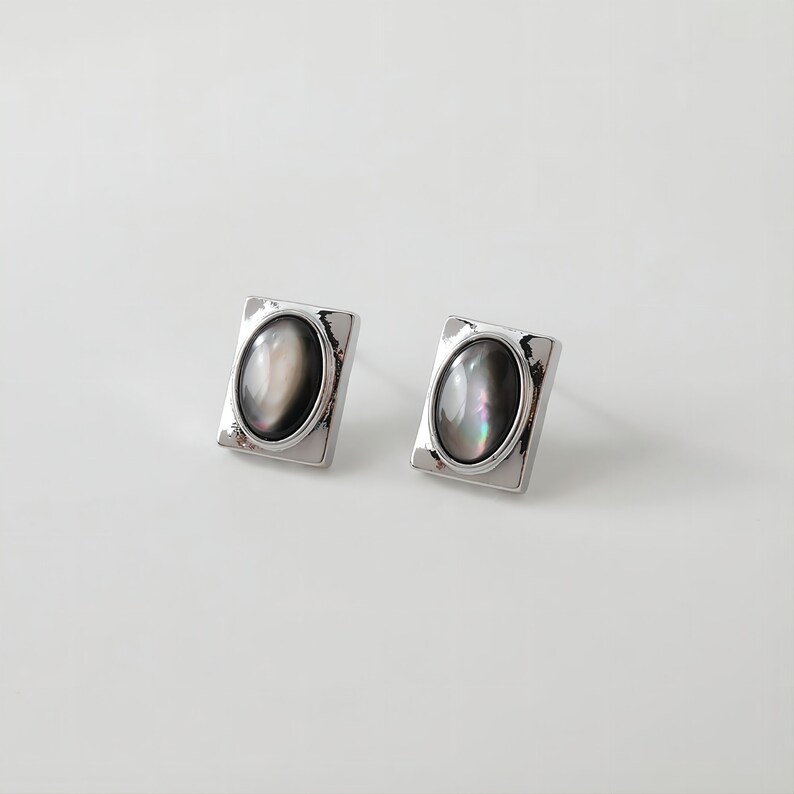 May include: A pair of silver earrings with a square setting and a black oval-shaped stone.