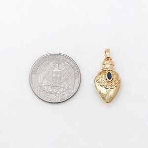 May include: A gold heart-shaped pendant with a blue gemstone in the center. The pendant is about the size of a US quarter.