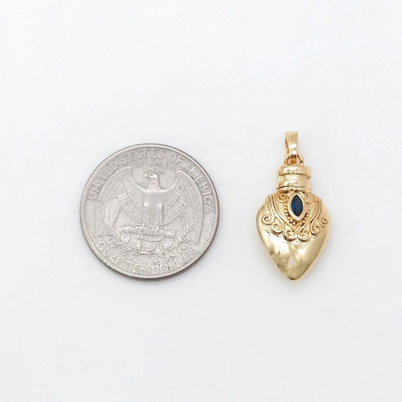May include: A gold heart-shaped pendant with a blue gemstone in the center. The pendant is about the size of a US quarter.