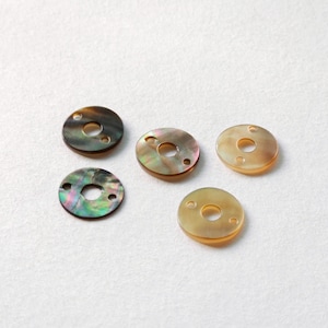 Könnte beinhalten: Fünf runde, irisierende Perlmutt-Scheiben mit einem Loch in der Mitte. Jede Scheibe hat zwei kleinere Löcher am äußeren Rand.
