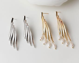 May include: Two pairs of earrings. One pair is silver-coloured, with three curved, elongated elements. The other pair is gold-coloured, with three similar elements, each adorned with small, dangling pearls. The earrings are displayed on a white surface.