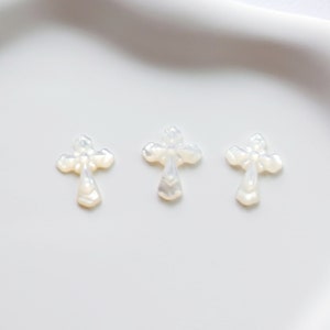 May include: Three white mother of pearl cross charms. The crosses are ornate and have a slightly iridescent sheen.