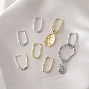 May include: A set of gold and silver hoop earrings with a rose and moon charm. The earrings are oval shaped and have a simple design.