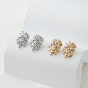 May include: Four earring findings in different finishes: silver, silver, gold, and gold. Each finding has a textured, square-shaped top and a loop for attaching an earring.