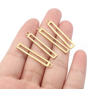 May include: Four gold-colored metal rectangular frames with a loop at the top. The frames are arranged in a stack, with the largest frame at the bottom and the smallest frame at the top.