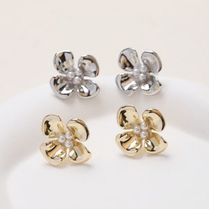 May include: A pair of flower-shaped earrings with a pearl center. One pair is gold and the other is silver.