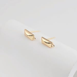 May include: A pair of gold-toned earring blanks with a rectangular shape and a small loop at the bottom. The blanks are designed for adding charms or other jewelry components.