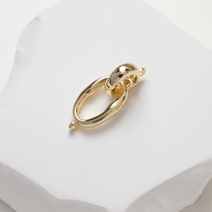 May include: Gold-toned metal connector with a smooth, oval shape. The connector has two loops for attaching jewelry pieces.