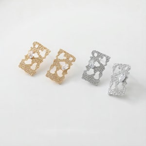 May include: Three pairs of earrings with a delicate, openwork design featuring a heart shape. The earrings are available in gold, silver, and rose gold.