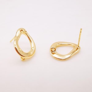 May include: A pair of gold-toned earrings with a unique, irregular oval shape. The earrings have a post back closure.