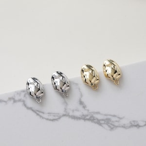 May include: Four metal charms in the shape of a wrinkled, abstract, organic form. Two charms are gold and two are silver.