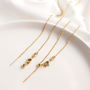 May include: Three gold chain extenders of varying lengths. The extenders are made of a delicate chain with a lobster clasp on one end and a small bead or loop on the other end.