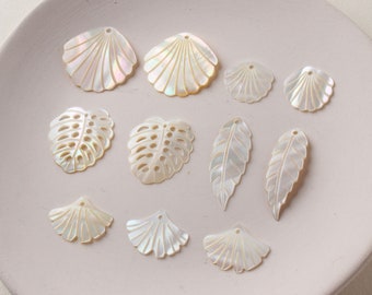 May include: A collection of white shell charms with various shapes, including leaves, fans, and seashells. The charms have a pearlescent finish and are perfect for jewelry making or crafting.