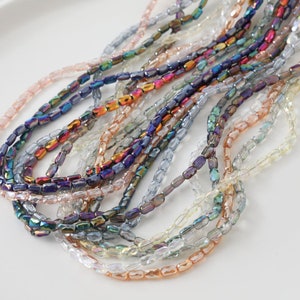 May include: A collection of iridescent glass beads in various colours, including blue, purple, pink, and clear. The beads are faceted and have a rectangular shape.